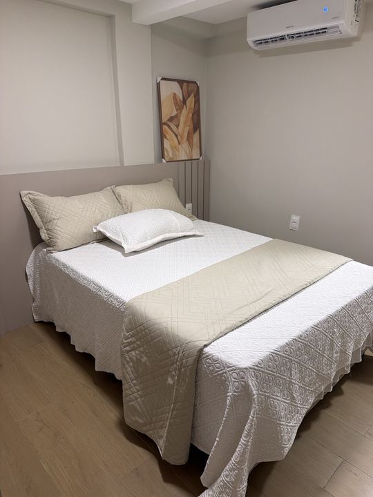 Cama de casal com manta bege, quadro e ar-condicionado